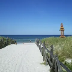 Ścieżka na piaszczystej plaży w Lubiatowie prowadzi do morza. Widoczny drewniany słup z tablicami informacyjnymi, jedna z nich to "Lubiatowo atrakcje".
