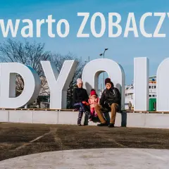 Rodzina pozuje na tle napisu GDYNIA. Idealne miejsce na weekendowe atrakcje w Gdyni.