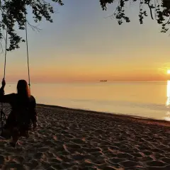 Zachód słońca nad morzem, dziewczyna na huśtawce na plaży.
