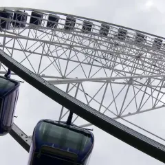 Widok z dołu na koło widokowe w Gdyni z ciemnoniebieskimi gondolami.