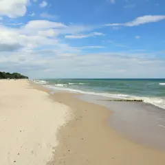 Szeroka, piaszczysta plaża w Gąskach, z zielonym lasem na klifie i spokojnym morzem.