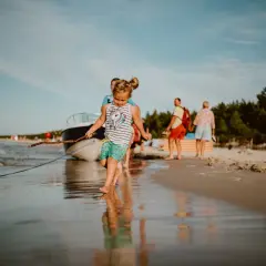 Dziewczynka z patykiem na plaży w Karwi. W tle łódź i ludzie, idealne karwia atrakcje dla dzieci.