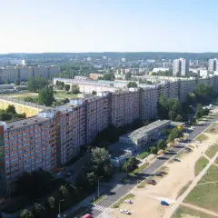 Długi, falisty budynek mieszkalny, znany jako falowiec gdańsk, ciągnie się przez krajobraz miejski, otoczony zielenią i innymi budynkami.