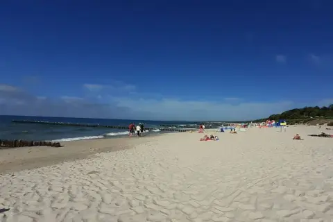 Słoneczna plaża wschodnia Ustka z ludźmi spacerującymi i odpoczywającymi na piasku.