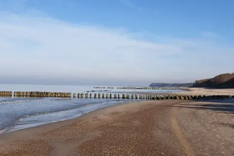 Plaża nad Bałtykiem z drewnianymi falochronami i łagodnymi falami.