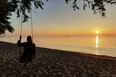 Zachód słońca nad morzem, dziewczyna na huśtawce na plaży.