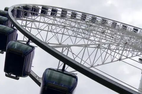 Widok z dołu na koło widokowe w Gdyni z ciemnoniebieskimi gondolami.