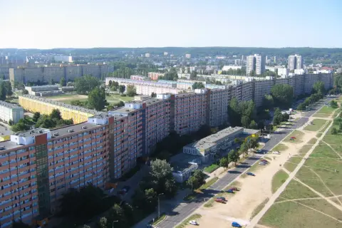 Długi, falisty budynek mieszkalny, znany jako falowiec gdańsk, ciągnie się przez krajobraz miejski, otoczony zielenią i innymi budynkami.