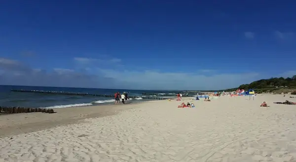 Słoneczna plaża wschodnia Ustka z ludźmi spacerującymi i odpoczywającymi na piasku.