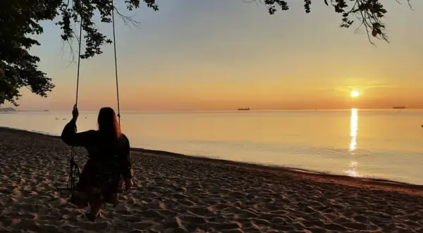 Zachód słońca nad morzem, dziewczyna na huśtawce na plaży.