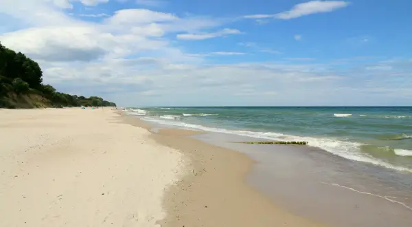 Szeroka, piaszczysta plaża w Gąskach, z zielonym lasem na klifie i spokojnym morzem.