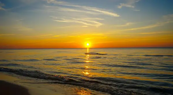 Piękny plaża zachód słońca nad spokojnym morzem. Słońce odbija się w wodzie, tworząc złoty szlak.