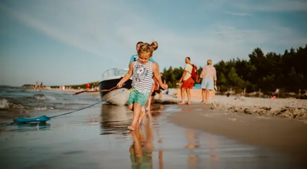 Dziewczynka z patykiem na plaży w Karwi. W tle łódź i ludzie, idealne karwia atrakcje dla dzieci.