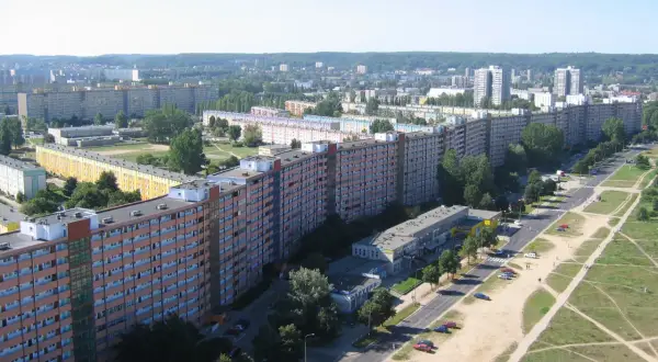 Długi, falisty budynek mieszkalny, znany jako falowiec gdańsk, ciągnie się przez krajobraz miejski, otoczony zielenią i innymi budynkami.