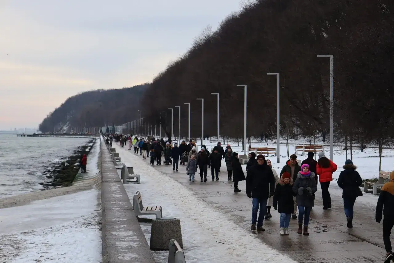 Spacerem po zaśnieżonym bulwarze w Gdyni, widać tłum ludzi spacerujących wzdłuż morza.