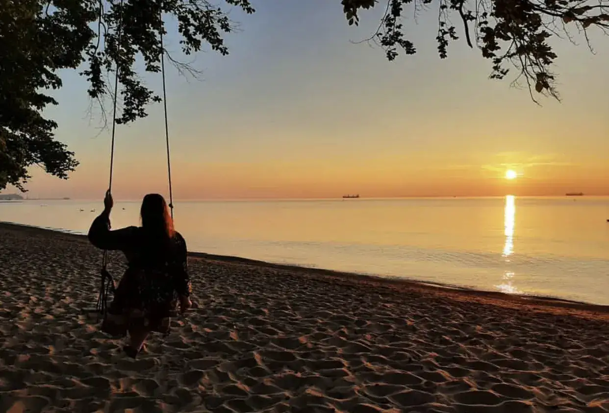 Zachód słońca nad morzem, dziewczyna na huśtawce na piaszczystej plaży.
