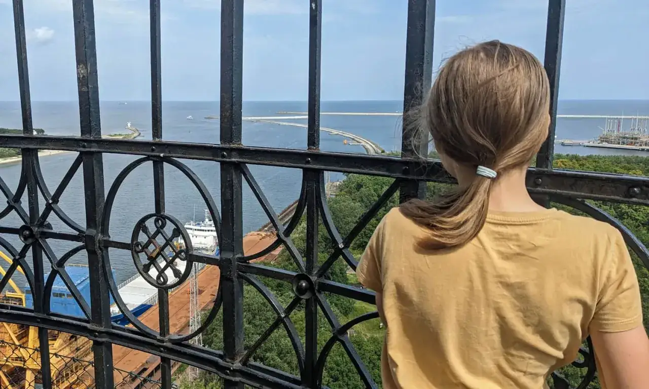 Widok z najwyższej latarni morskiej w Polsce. Dziewczynka w żółtej koszulce podziwia morze i port.