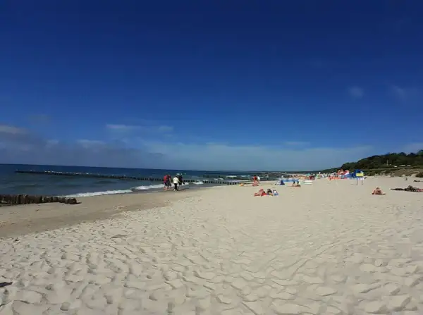 Słoneczna plaża wschodnia Ustka z ludźmi spacerującymi i odpoczywającymi na piasku.