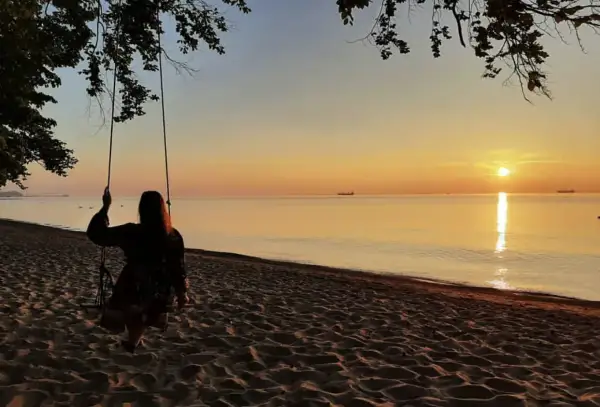 Zachód słońca nad morzem, dziewczyna na huśtawce na plaży.