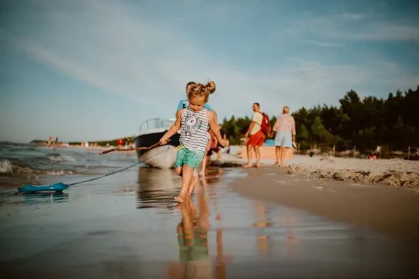 Dziewczynka z patykiem na plaży w Karwi. W tle łódź i ludzie, idealne karwia atrakcje dla dzieci.