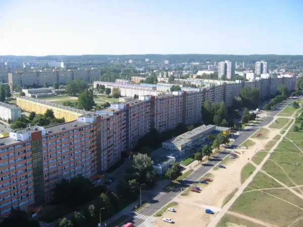 Długi, falisty budynek mieszkalny, znany jako falowiec gdańsk, ciągnie się przez krajobraz miejski, otoczony zielenią i innymi budynkami.